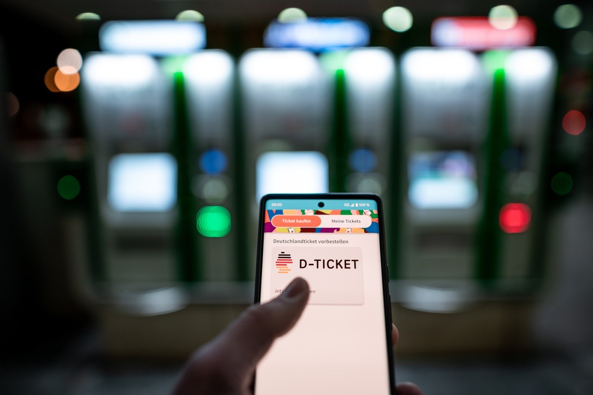 03.04.2023, Nordrhein-Westfalen, Essen: Ein Mann hält ein Mobiltelefon, auf dem das "D-Ticket" gekauft werden kann, vor Ticketautomaten am Hauptbahnhof Essen in der Hand. Am Montag beginnt d ...
