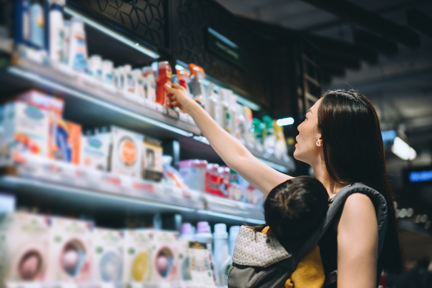 Young Asian mother grocery shopping with little daughter and choosing for baby necessities in a store