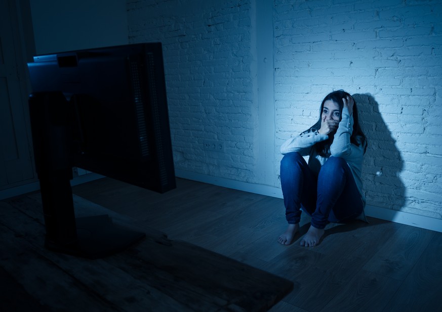 Dramatic portrait of sad scared young woman sitting on the ground staring a computer suffering bullying and harassment. Being online abused by stalker feeling desperate in Internet problem concept.