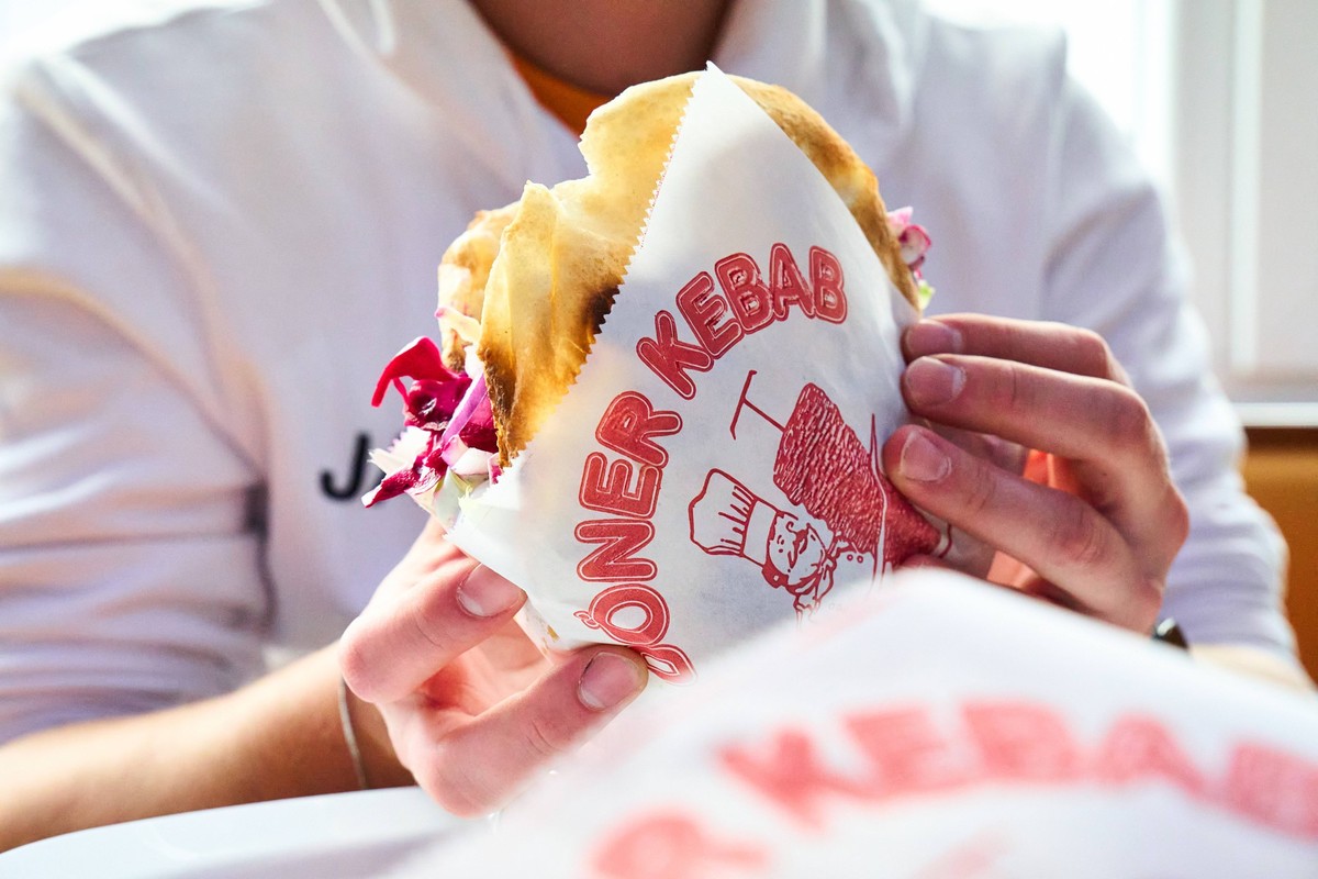Karlsruhe, Baden-Württemberg, Germany - March 4, 2025: Man holding a doner kebab in a printed doner kebab wrapper. Fast food dish in a restaurant or snack bar. Typical street food with meat, salad and ...