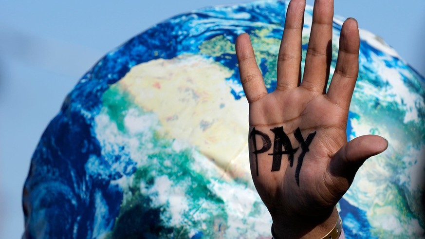 ARCHIV - 18.11.2022, Ägypten, Scharm el Scheich: Auf einer Hand ist &quot;Pay&quot; zu lesen, die auf dem UN-Klimagipfel COP27 bei einem Protest der Entschädigungen für Verluste und Schäden fordert. F ...
