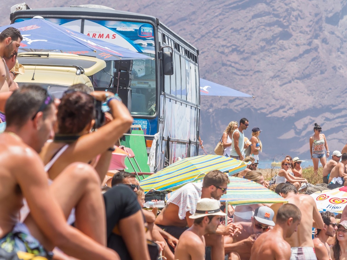 TENERIFE, SPAIN 11- AUGUST- 2013: groups of several people spending the day on the beach, with umbrellas and in bathing suits, sunbathing, taking a swim on the beach and watching the bodyboard champio ...