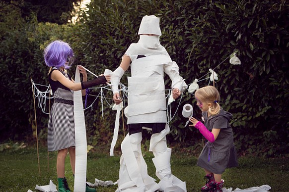 Two children wrapping a third child with toilet paper to play 'Mummy Wrap' Halloween game