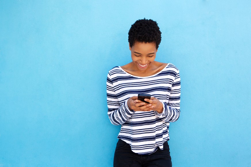 Portrait of happy black woman looking at mobile phone by blue background