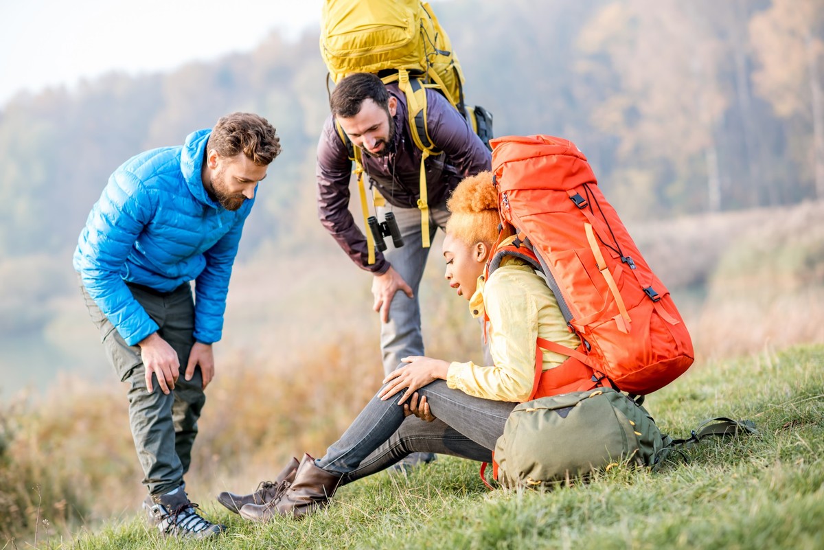 Young african woman with backpack having a trauma with knee hiking with friends outdoors