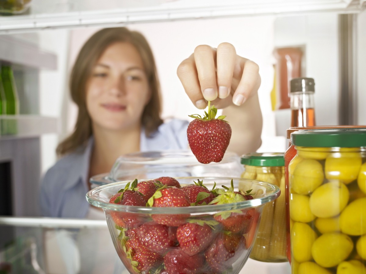 Young lady taking strawberry from a fridge