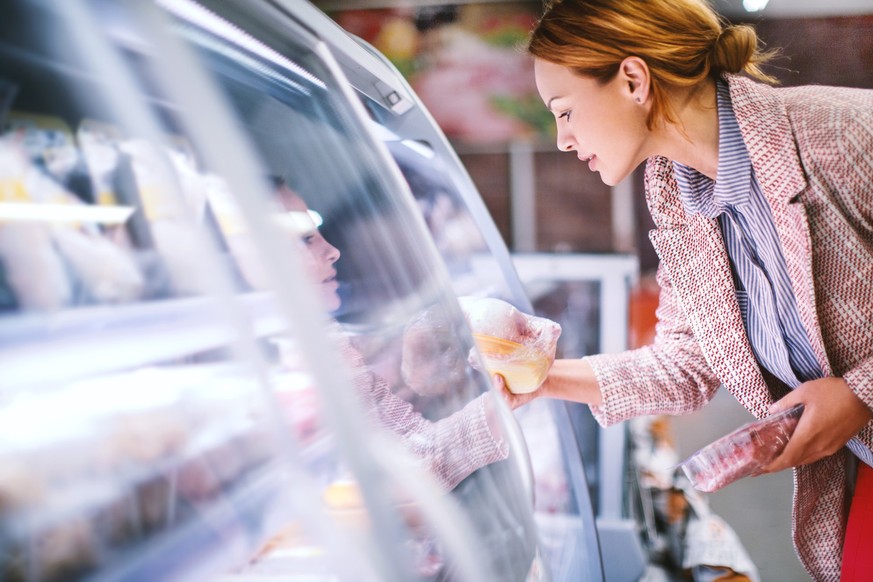 Attractive smiling brunette taking meat from a fridge at local supermarket. Side view. Horizontal.