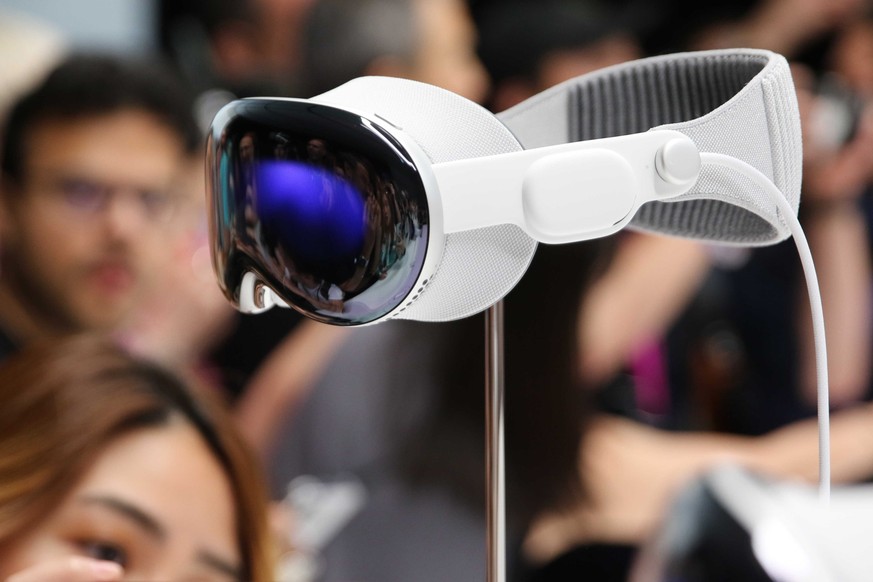 ARCHIV - 05.06.2023, USA, Cupertino: Medienvertreter und Blogger umlagern die Computerbrille Apple Vision Pro, die im Steve Jobs Theater auf dem Apple-Firmencampus in Cupertino ausgestellt wird. (zu d ...