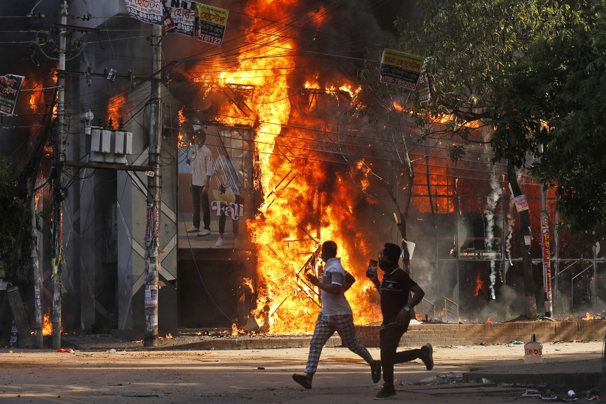 Men run past a shopping center which was set on fire by protesters during a rally against Prime Minister Sheikh Hasina and her government demanding justice for the victims killed in the recent country ...