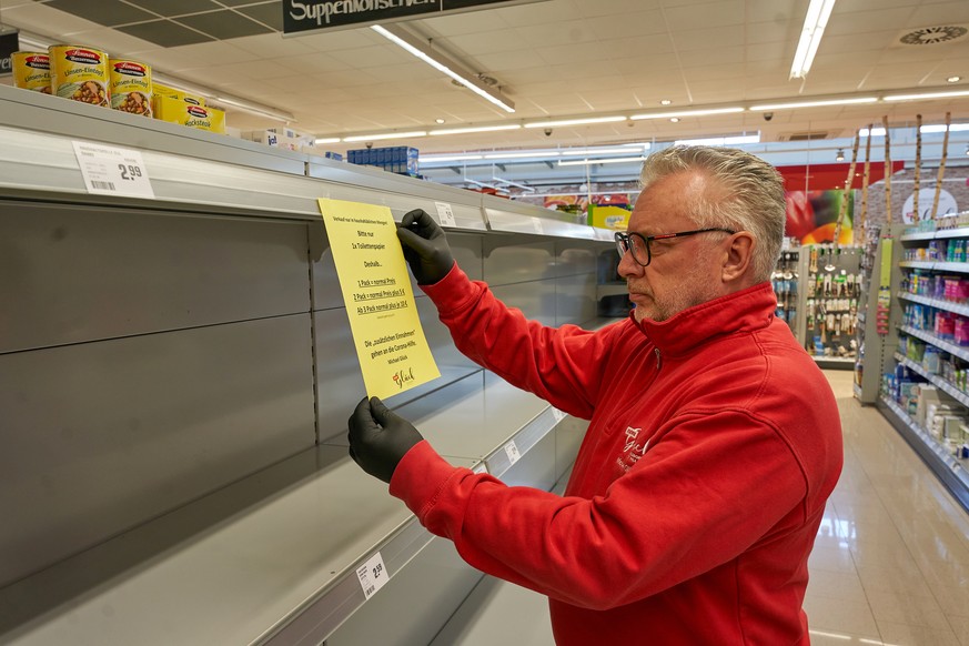 21.03.2020, Rheinland-Pfalz, Rengsdorf: Supermarktbetreiber Michael Glück bringt an dem für das Toilettenpapier vorgesehenen Regal ein Schild an, das die Kunden darauf hinweist, dass die erste Packung ...