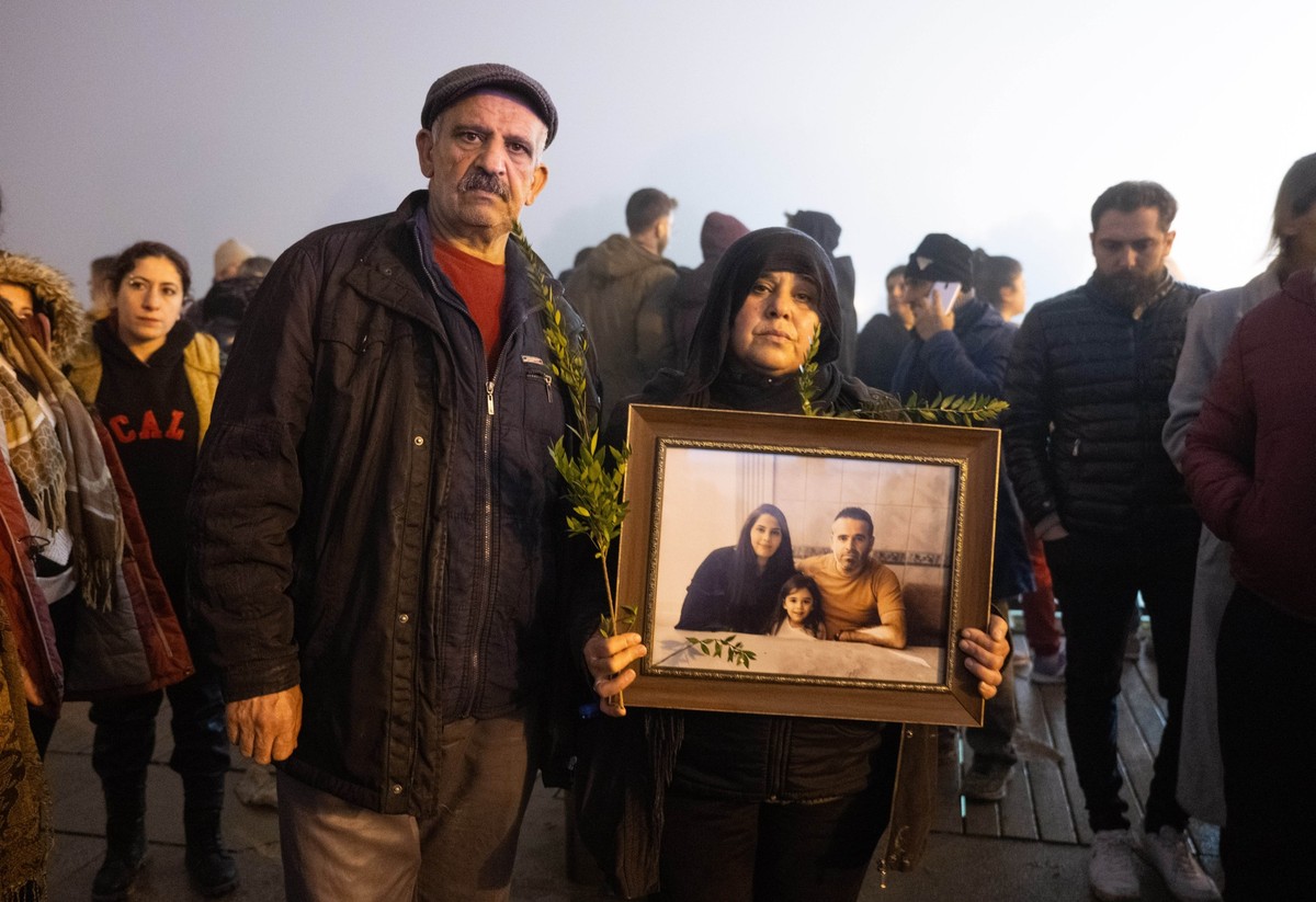 06.02.2024, Türkei, Antakya: Mit einem Bild ihrer, beim Erdbeben ums Leben gekommenen Verwandten, ist dieses Ehepaar in den frühen Morgenstunden am Jahrestag des Bebens zu einer Kundgebung gekommen. V ...