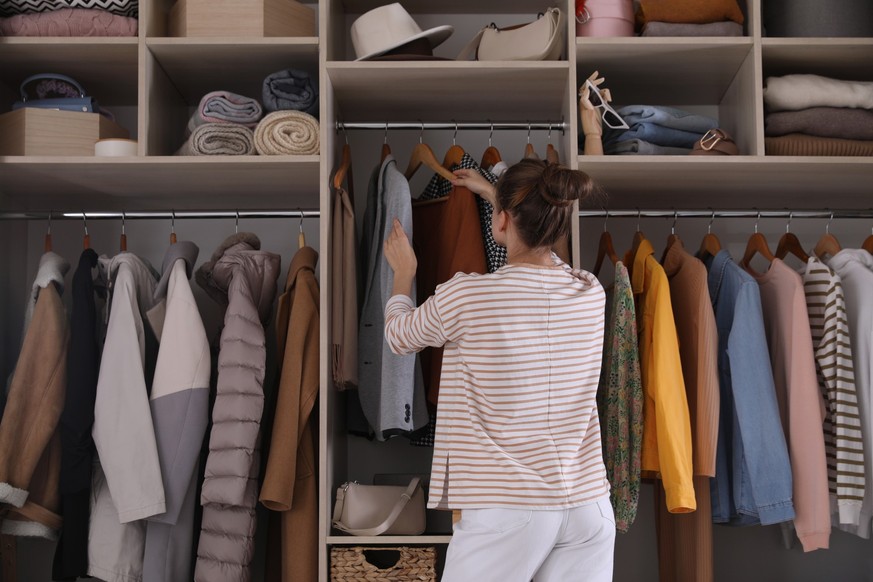 Young woman choosing clothes in wardrobe closet, back view