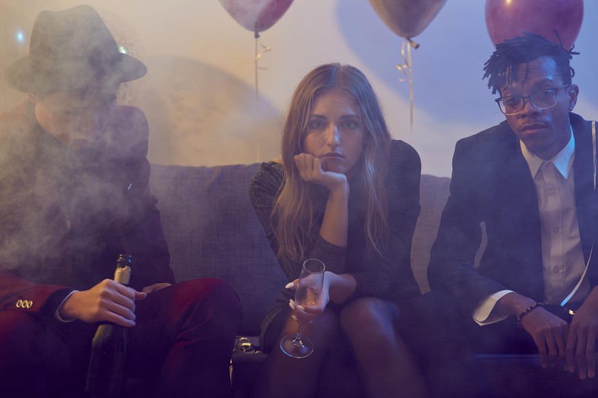 Portrait of drunk young woman holding champagne glass while siting on sofa during party in smoky nightclub