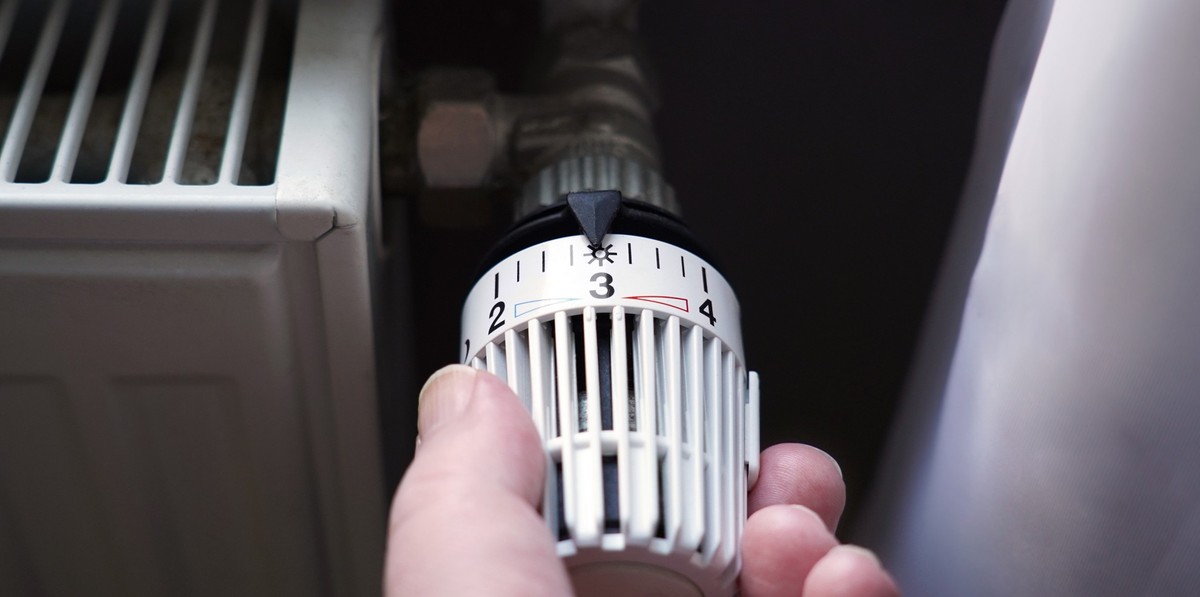hand turning down thermostat on radiator to save energy due to heating cost price hike