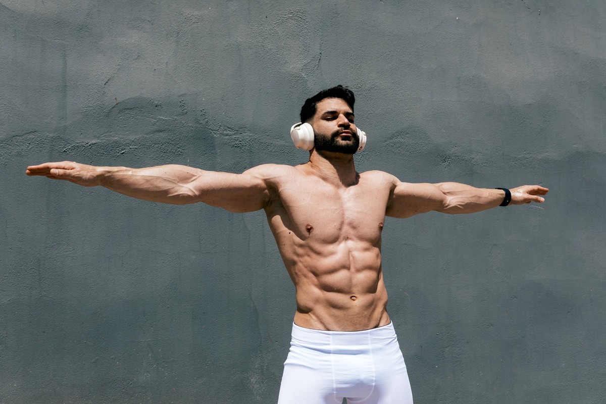 MR_ID30450_22335_MaiquelGomezAnton.jpg A fit man stands confidently with arms outstretched, headphones on, under the sunlight. His toned physique and focused expression epitomize health, fitness, and  ...