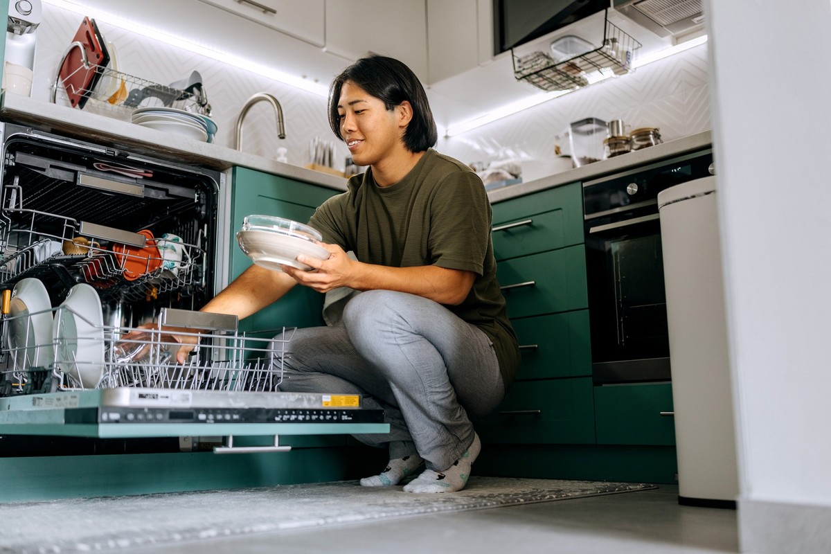 Young casually clothed man unloading dishwasher machine