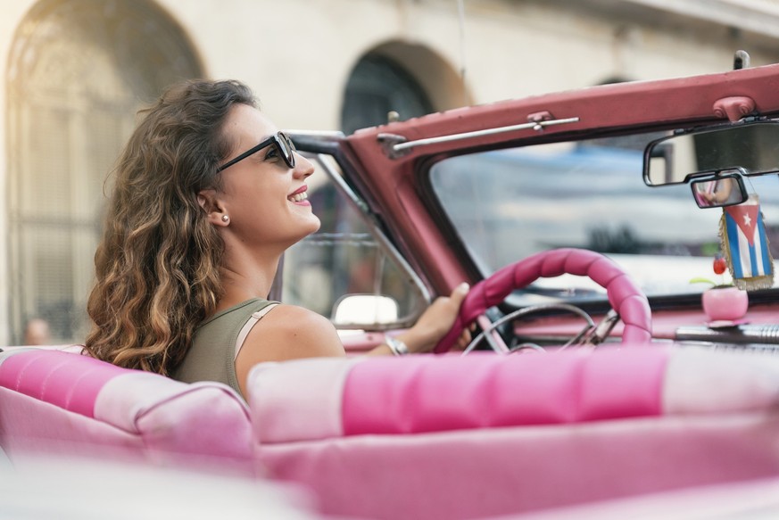 Beautiful woman tourist enjoying vacation holidays in Cuba driving a classic car.