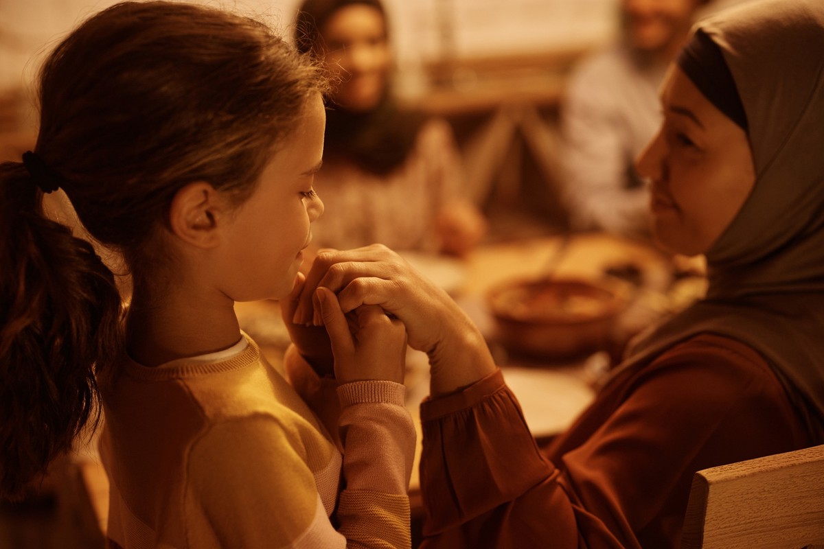 Middle Eastern granddaughter holding grandmother&#039;s hand during family dinner at dining table.