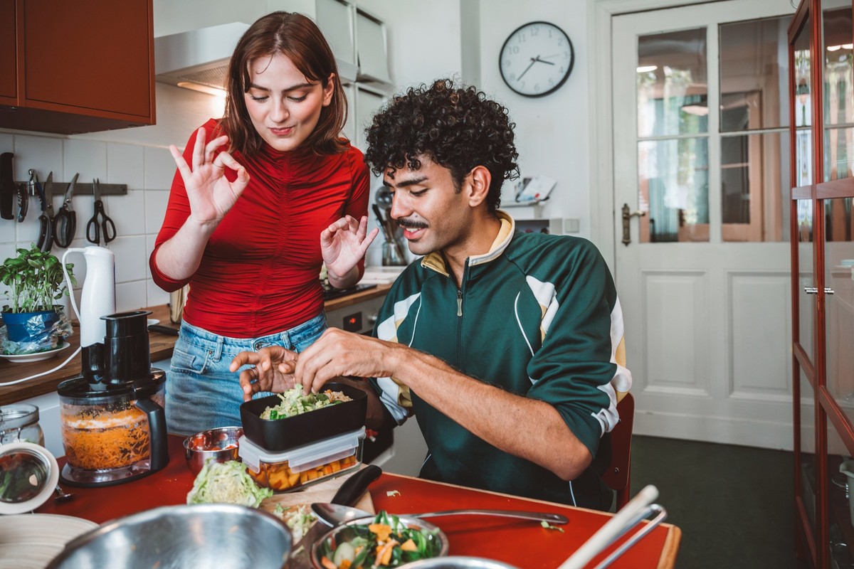 young woman and man packing snack boxes with prepared food in kitchen