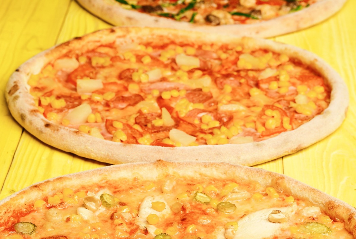 Italian pizza and pizzeria concept. Hawaii pizza with meat, corn, tomatoes and cheese on yellow wood background. Take away food with various ingredients and crunchy edges. Different pizza set for menu ...