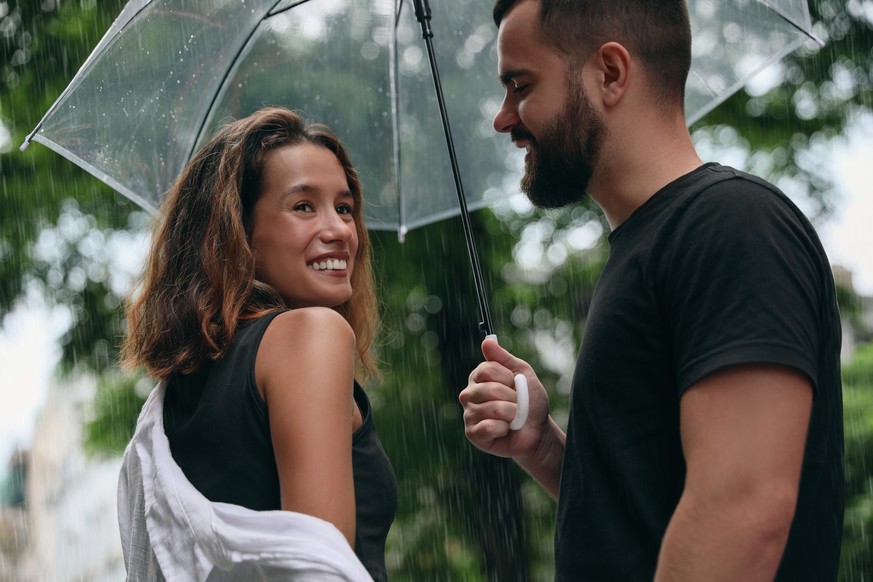 Young couple with umbrella enjoying time together under rain on city street Dating Date Regen Liebe Paar Regenschirm schlechtes Wetter nass