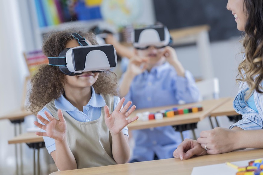 Young private schoolgirl gestures while using virtual reality goggles at school.