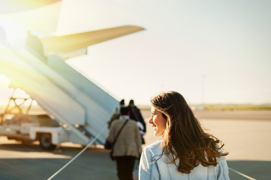 Woman tourist passenger getting in to airplane at airport, walking from the terminal to the plane.