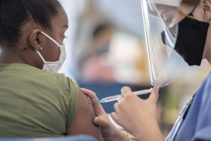 School nurse administering a vaccine to a masked student.