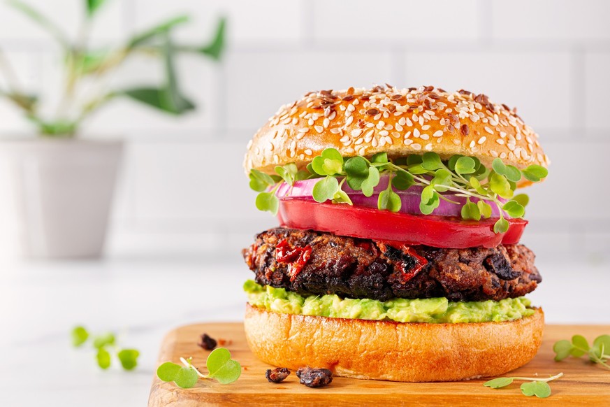 Plant based black bean avocado burger on sesame seed bun with tomato, microgreens and red onion