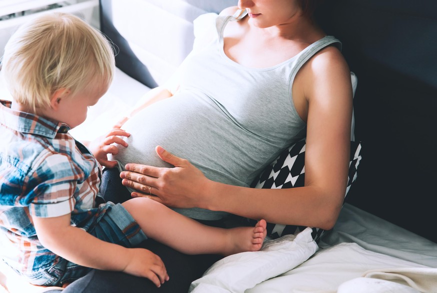 Pregnant mother and son are talking and spending time together in bed at home. Little child boy looking at her mother pregnant tummy. Pregnancy, family, parenthood, preparation and expectation concept ...