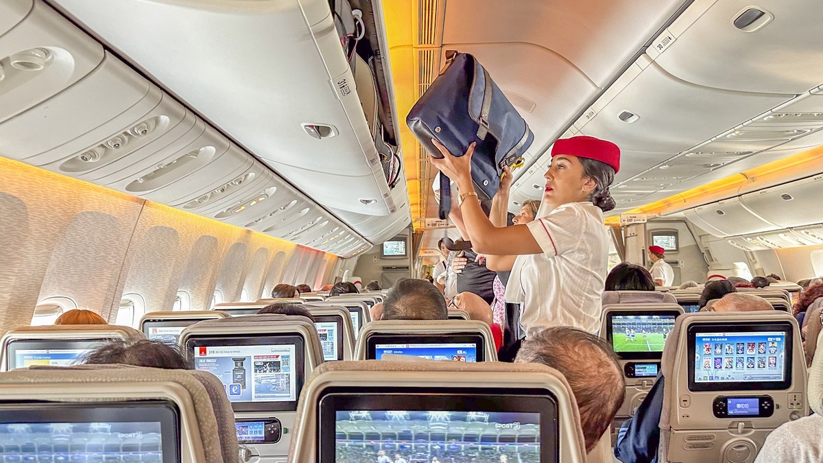 DUBAI,UAE. 16 SEPTEMBER 2023. Passenger seated, stewardess stows baggage, a seamless start to the airborne voyage Model Released Property Released xkwx crew crowded sit uniform friendly public class s ...