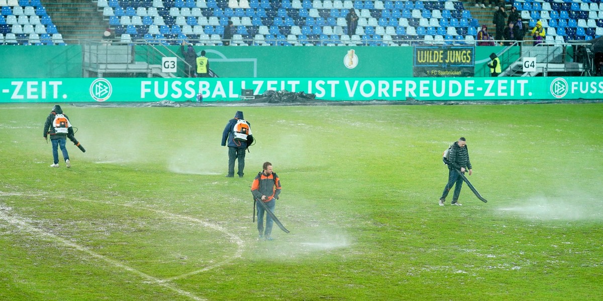 07.02.2024, Saarland, Saarbrücken: Fußball: DFB-Pokal, 1. FC Saarbrücken - Bor. Mönchengladbach, Viertelfinale im Ludwigspark-Stadion. Arbeiter versuchen, Wasserlachen vom Spielfeld zu entfernen. Ande ...