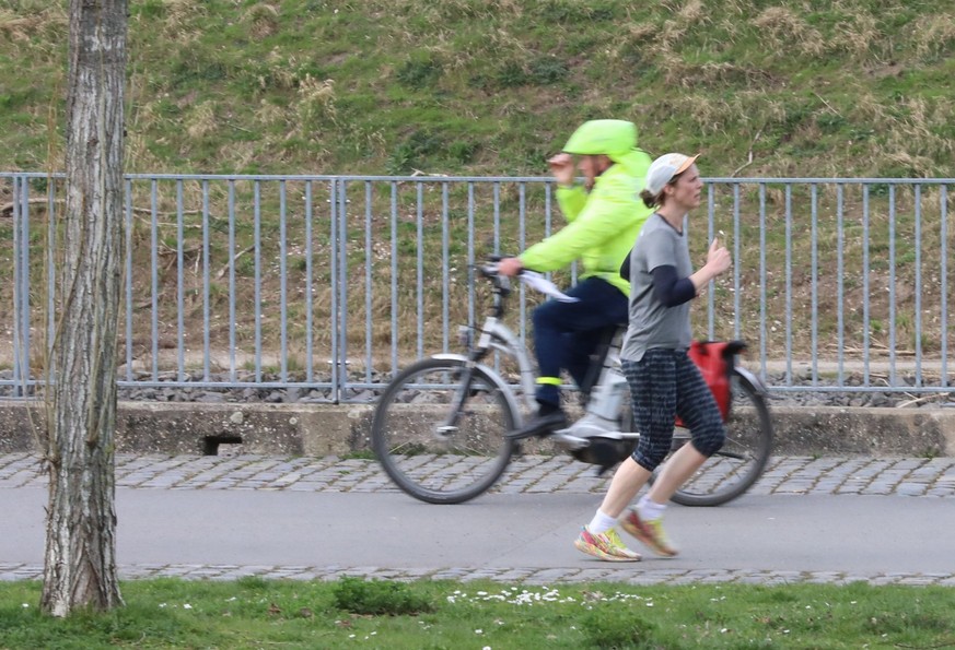 10.03.2024, Nordrhein-Westfalen, Köln: Gegensätze: Eine Joggerin läuft in T-Shirt und Shorts an einem Radfahrer mit Regenjacke vorbei. Laut Vorhersage der Meteorologen verabschiedet sich das schöne Fr ...