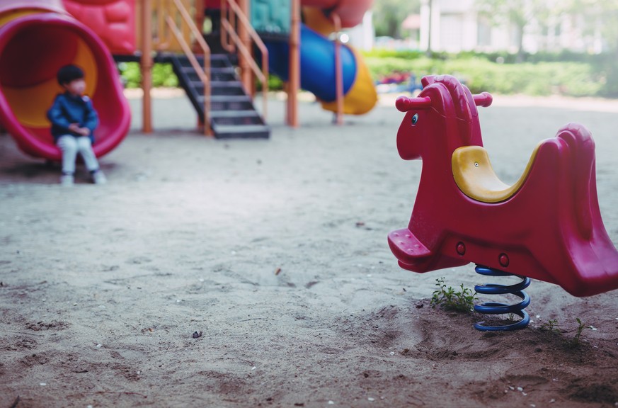 little boy is playing lonely in playground. little boy is sitting unhappy in playground.