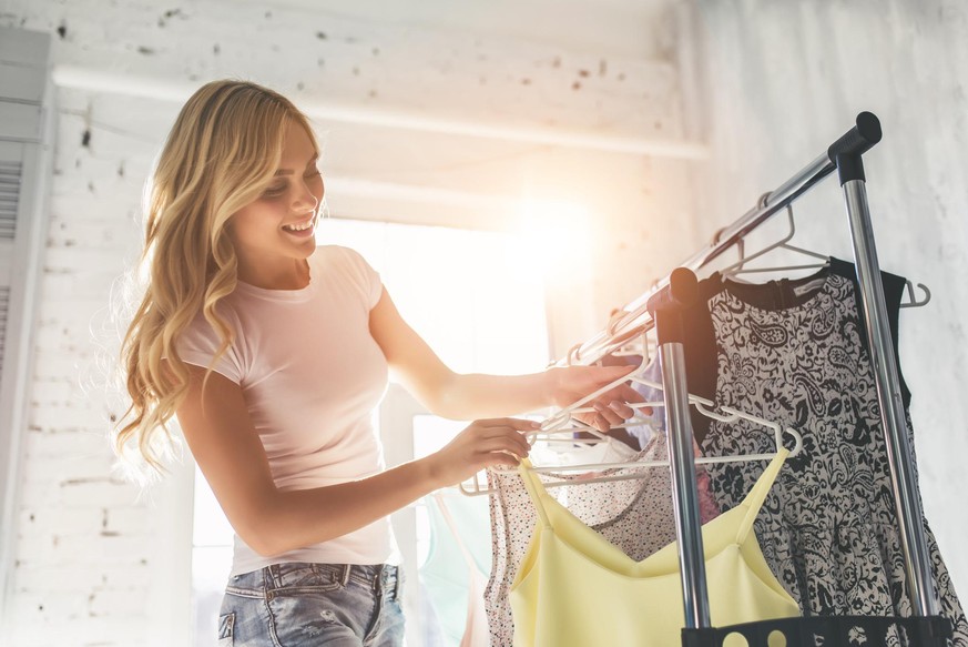 Attractive young woman is choosing clothes in light room. Girl in wardrobe.