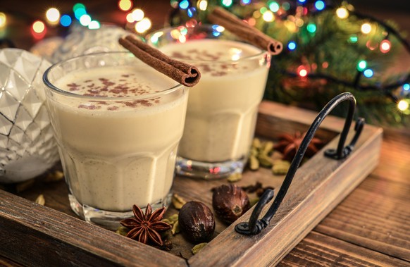 Traditional christmas drink eggnog in glass with spices and christmas lights on wooden background