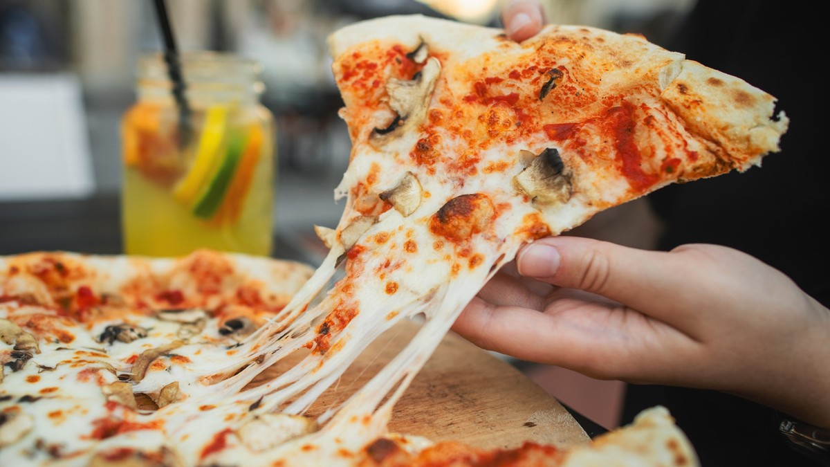 Close-up of a woman&#039;s hand taking a slice of delicious pizza with stretching cheese in a pizzeria restaurant
