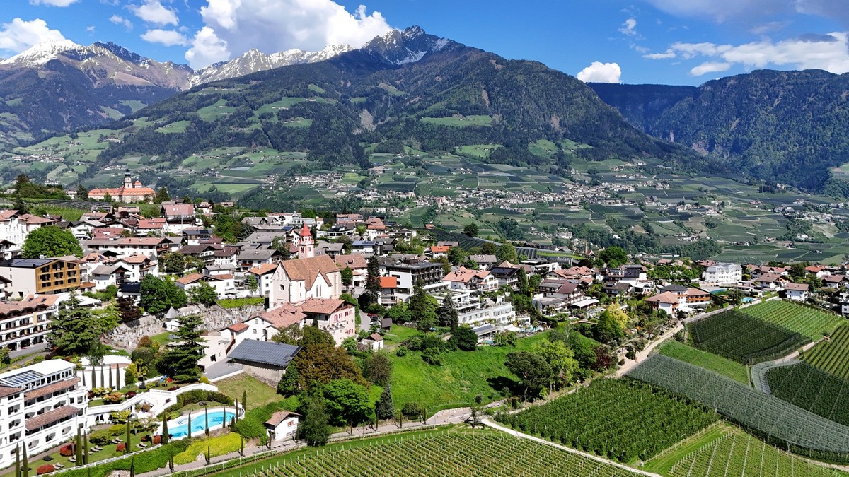 Ein Frühlingstag, Frühsommertag in Dorf Tirol bei Meran, Tirolo. Hier der Blick auf die Ortschaft mit Häusern, Hotels, der Pfarrkirche Hl. Johannes der Täufer, im Hintergrund Schenna und der Ifinger,  ...