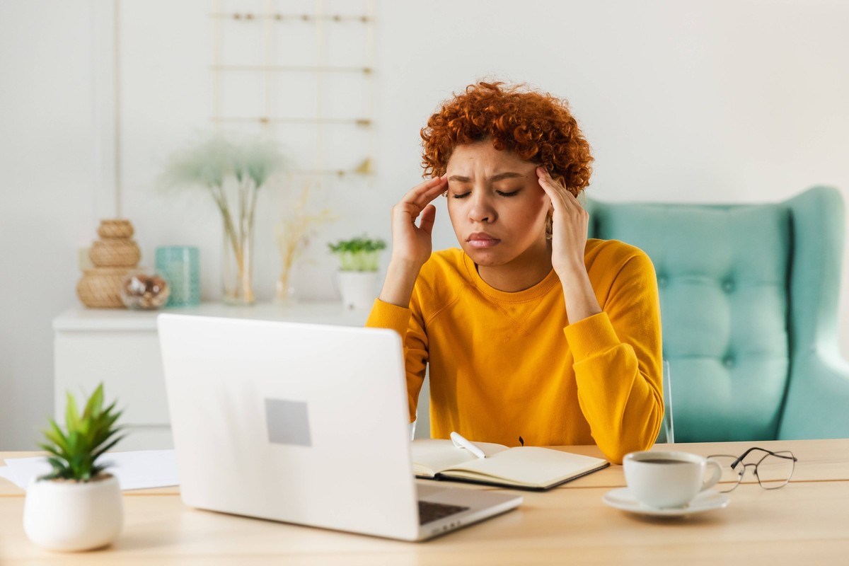 African woman touching temples experiencing stress. Girl at home office tired of working feeling headache sick rubbing temples forehead. Long laptop usage computer vision syndrome. Office syndrome. Af ...