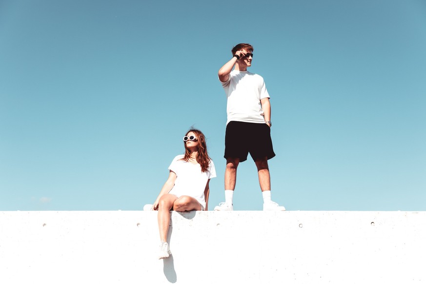 Modern Urban Fashionable Lifestyle Young Couple Portrait. Young man and woman on concrete wall wearing sunglasses looking in opposite directions. Modern Couple Lifestyle Portrait. Edited Colors.