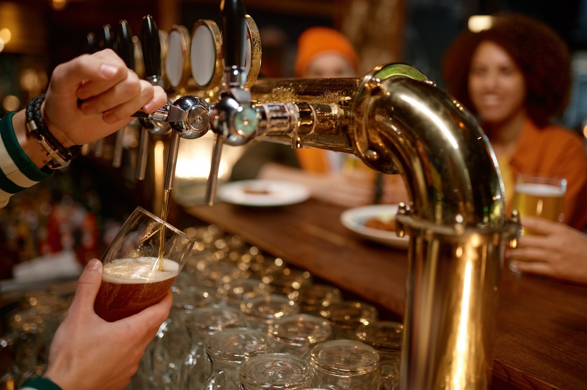 Closeup bartender hands filling glass with beer for group of friends, Closeup bartender hands filling glass with beer for group of friends sitting at bar counter desk. Millennial multiracial young peo ...