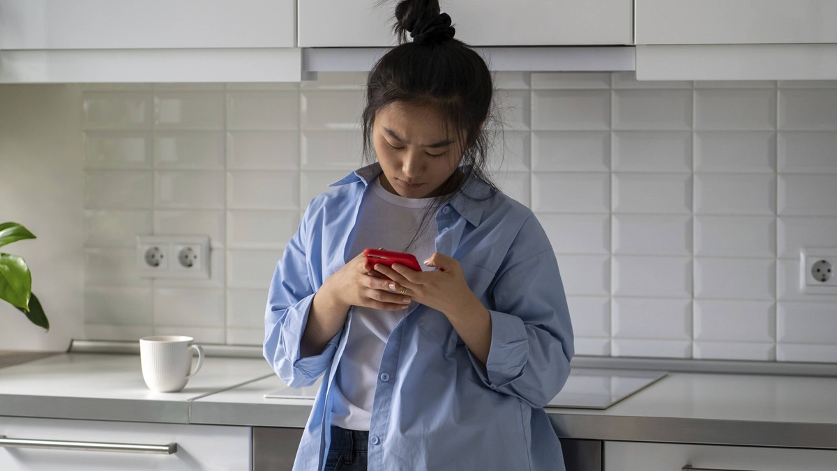 Stirnrunzelnd verärgert asiatische junge Frau hält Smartphone erhalten Nachricht oder E Mail mit schlechten Informationen. Upset verwirrt chinesische Mädchen sieht auf Handy sehen wichtigen Anruf verp ...