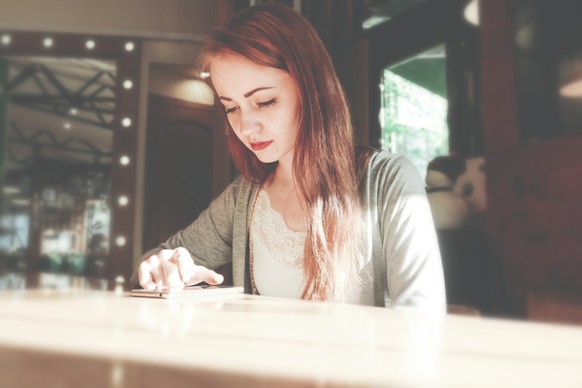 beautiful girl sits in a cafe and writes sms on her mobile phone