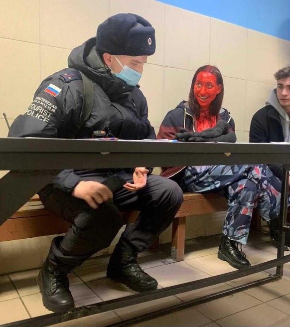 Das Gesicht und Dekolleté voller Kunstblut sitzt Polina Oleinikova mit einem Polizisten auf dem Polizeirevier.  