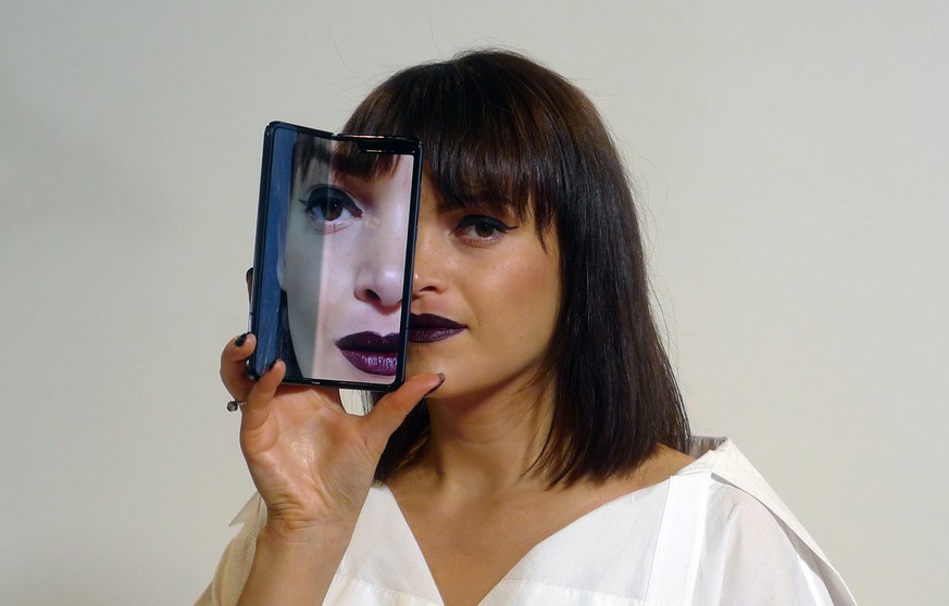 A model holds a Samsung Galaxy Fold smartphone to her face, during a media preview event in London, Tuesday April 16, 2019. Samsung is hoping the innovation of smartphones with folding screens giving  ...