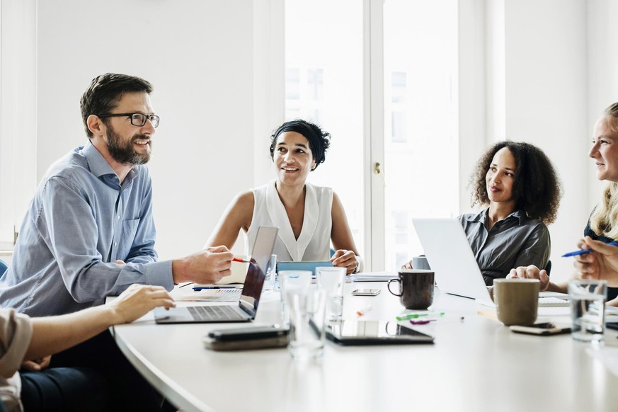 An office manager sitting at a large desk and talking to his employees during a morning meeting.