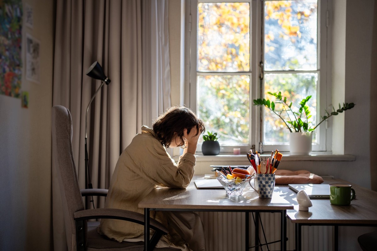 Gestresste Frau mit Burnout sitzt am Tisch und hält den Kopf mit den Händen, die sich schlecht fühlen, weil sie ein Arbeitsproblem hat Exhausted depressed woman with professional burnout sitting at ta ...