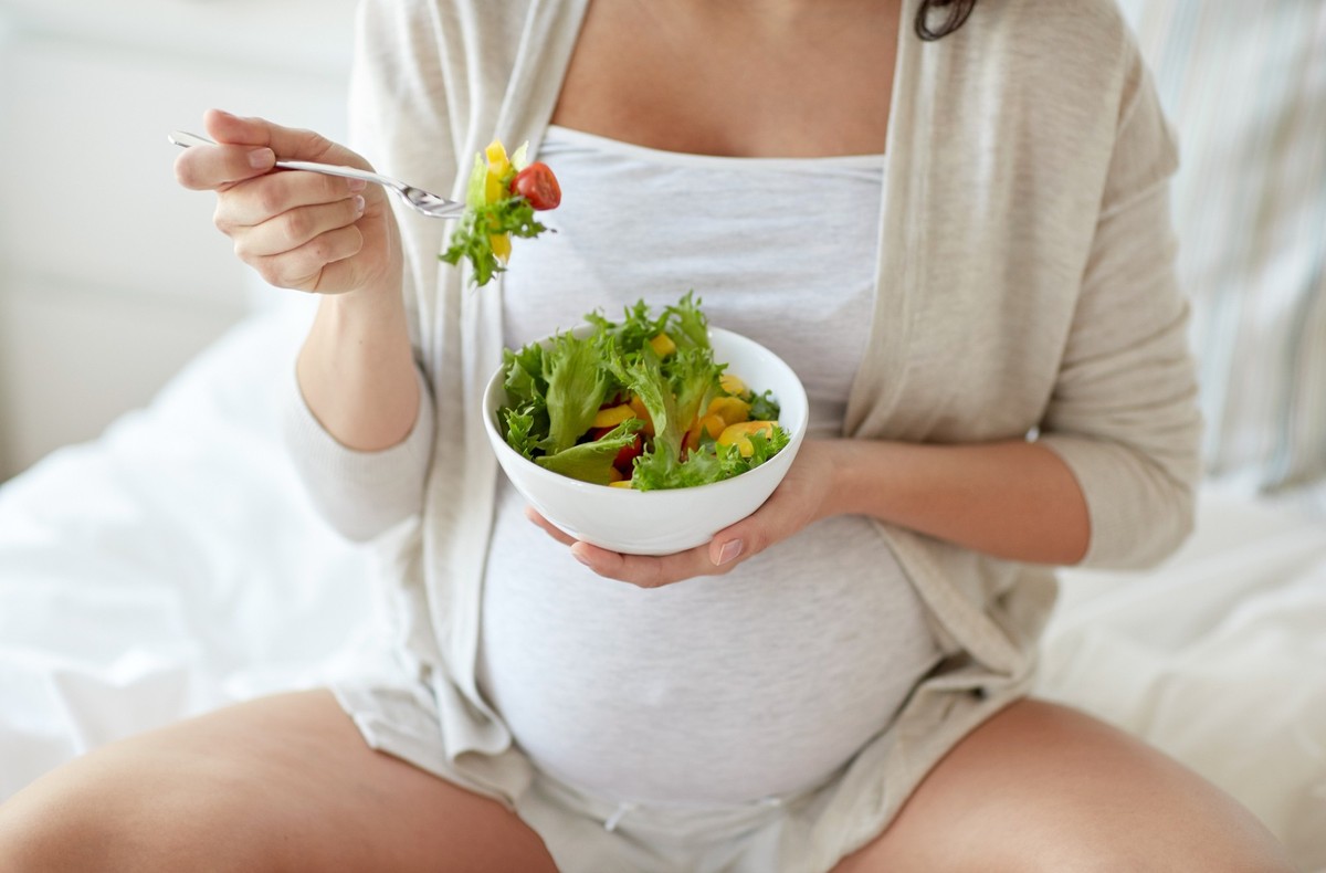 pregnancy, healthy food and people concept - close up of happy pregnant woman eating vegetable salad for breakfast in bed at home