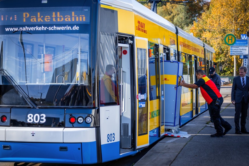 28.10.2022, Mecklenburg-Vorpommern, Schwerin: Ein Mitarbeiter der Deutschen Post schiebt einen Transportwagen für Pakete in eine Straßenbahn des Schweriner Nahverkehr. Die Deutsche Post hat ein Pilotp ...