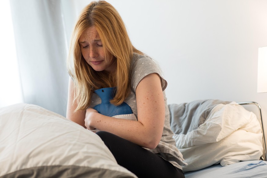 ILLUSTRATION - Eine junge Frau liegt am 18.09.2019 in einer Wohnung in Hamburg in einem Bett und leidet unter Regelschmerzen (gestellte Szene). Foto: Christin Klose || Modellfreigabe vorhanden